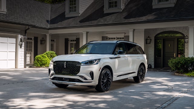 A white 2026 Lincoln Aviator® SUV is parked in the driveway of a luxury home. | Deacon Jones Lincoln in Goldsboro NC