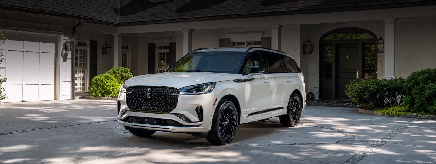 A white 2026 Lincoln Aviator® SUV is parked in the driveway of a luxury home. | Deacon Jones Lincoln in Goldsboro NC