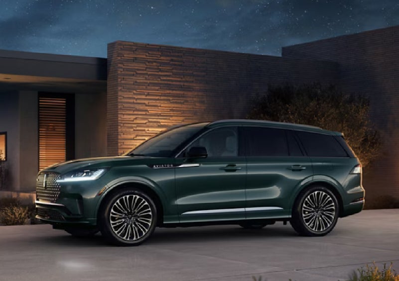 A green 2027 Lincoln Aviator® SUV is parked outside a contemporary home. | Deacon Jones Lincoln in Goldsboro NC