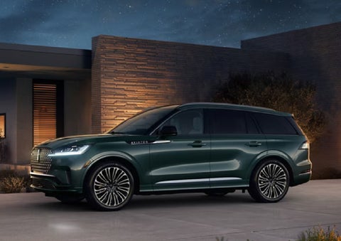 A green 2027 Lincoln Aviator® SUV is parked outside a contemporary home. | Deacon Jones Lincoln in Goldsboro NC