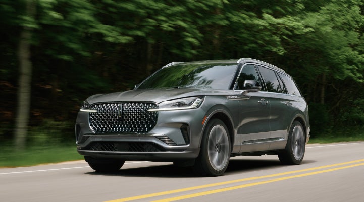 A 2027 Lincoln Aviator® SUV is being driven down a road lined with trees. | Deacon Jones Lincoln in Goldsboro NC